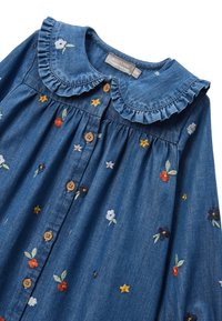 Robe en denim avec un col volanté, des boutons en bois et des broderies florales multicolores sur un fond bleu foncé.