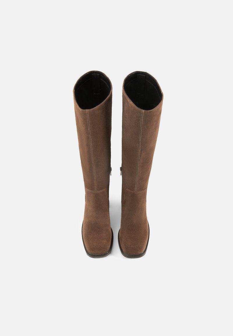 Brune ruskindsstøvler til knæene med en glat tekstur, firkantet tå og minimale syninger. Indersiden er sort med en ren finish.