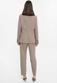 Gebraunierter Anzug mit einem maßgeschneiderten Blazer und geraden Hosenbeinen. Das Material hat eine strukturierte Oberfläche. Mit Knöpfen an den Manschetten.