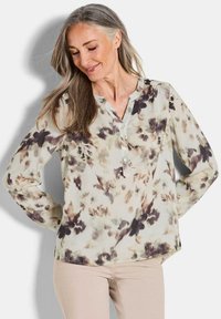 Floral Hemdbluse aus leichtem Material. Mit V-Ausschnitt, langen Ärmeln und schattierten Beigetönen, Braun und Olivgrün in sanften, gedämpften Mustern.