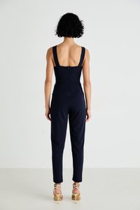 Λίκνο ναυτικού χρώματος με εφαρμοστή μπλούζα και φαρδιές τιράντες, με χαμηλή πλάτη και στενά παντελόνια. Φορεμένο με μπεζ ψηλοτάκουνα σανδάλια με λουράκια.