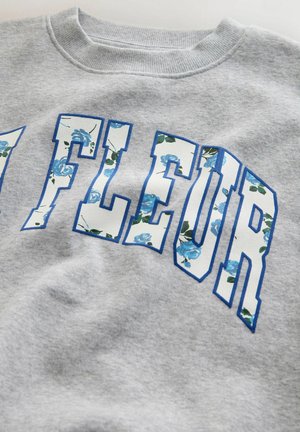 Sweat-shirt gris avec de grosses lettres bleues ornées de motifs floraux dans des nuances de bleu et de vert. Texture douce avec un col côtelé.