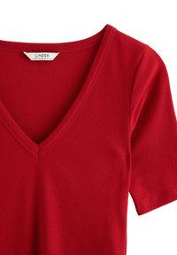 Červené krátké tričko s ribbed vzorem a výstřihem do V. Vyrobeno z měkké tkaniny, má přiléhavý střih a pečlivé švy podél okrajů.