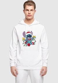 Felpa bianca con cappuccio che presenta una grafica colorata di un personaggio dei cartoni animati con un cappello da Babbo Natale, circondato da luci di Natale e decorazioni.