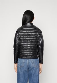 Svart puffy-jacka med quiltad textur, hög krage och långa ärmar. Kombinerad med högmidjade blå jeans som visar en elegant design.