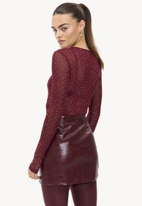 Bordeauxlang T-shirt met witte stippen, gecombineerd met een hoogwaisted, glanzende bordeaux nep leren minirok. Soepele textuur, getailleerd ontwerp.
