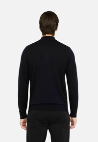 Maglione in maglia navy con maniche lunghe, orlo e colletto a coste. Texture liscia con branding minimale visibile sul retro.