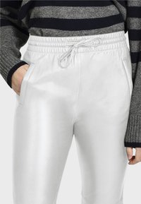 Witte elastische taillebandbroeken met zakken, voorzien van een gladde, glanzende afwerking en een koordsluiting, gecombineerd met een grijs gestreepte trui.