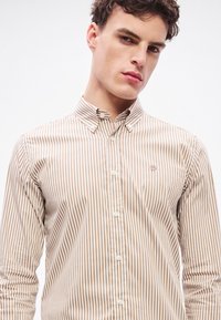 Hnedá a krémová pruhovaná košeľa na zapínanie s golierom, s malým logom na hrudi a hladkým, priliehavým strihom.
