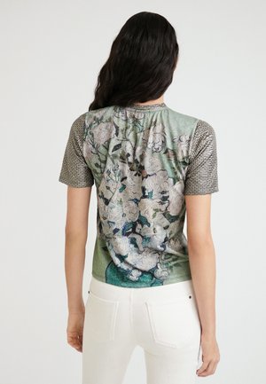 T-shirt à manches courtes avec un design floral aux couleurs pastel sur un dos texturé vert, et des manches en tissu gris à motifs.