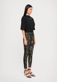 Black cropped t-shirt with gold text, paired with form-fitting black leggings featuring a textured brown and gold pattern. Black strappy heels.