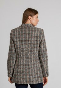 Blazer de cuadros gris hecho de tejido texturizado, con un corte entallado y solapas con muesca, con toques de marrón y blanco en el patrón.