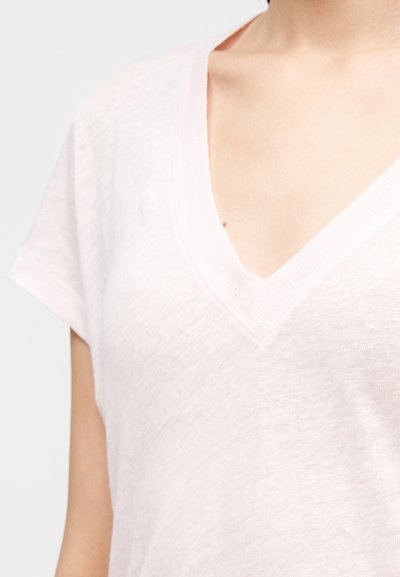 Tricou roz deschis cu decolteu în V, dintr-un material moale și texturat. Mâneci scurte și croială lejeră, cu un detaliu cusut la nivelul gâtului.