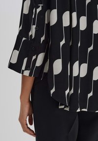 Camicia a motivi neri e crema con una vestibilità ampia, dotata di un orlo arrotondato e maniche arrotolate fissate con bottoni. Tessuto morbido.