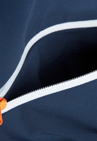 Marinblå tygväska med insidan i vitt, orange dragband och en vit dragkedja, med slät textur och strukturerad form.