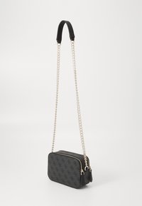Sac à main rectangulaire noir avec motif en relief, extérieur en tissu, bandoulière en chaîne argentée amovible, et accents en matériel doré. Fermeture zippée.
