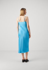 Satin sinine sättekleit õhukeste rihmadega, keskmise sääreni ulatuv, sile tekstuur ja kergelt kaarjas äär. Mustad plokknõelad.