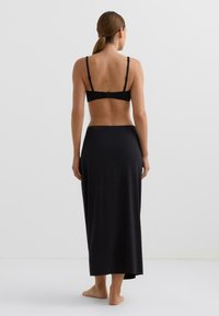 Črni oprijeti modrček z nastavljivimi naramnicami in zapenjanjem z zatičem na hrbtu, v kombinaciji z dolgo, tekočo črno krilo, izdelano iz mehke in gladke tkanine.