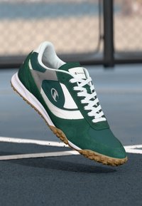 Tenis verde din suede cu accente albe, talpă din cauciuc și textură antiderapantă. Are șireturi și un logo stilizat pe lateral.