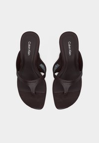Καφέ σκούρα δερμάτινα σανδάλια τύπου σφήνα Calvin Klein με τετράγωνη μύτη και επωνυμομένα πέλματα, εμφανιζόμενα από πάνω σε λευκό φόντο.