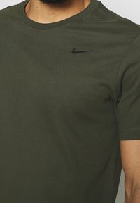 Camiseta de cuello redondo en verde oliva, hecha de algodón, con mangas cortas y un logo negro de Nike en la parte superior del pecho izquierdo.