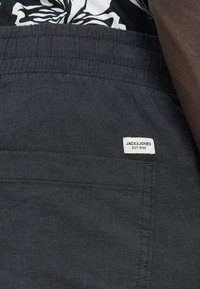 Σορτς σε σκούρο γκρι ύφασμα με υφή, με ελαστική μέση και μια μικρή λευκή ετικέτα που αναγράφει «JACK & JONES EST. 1990.»