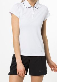 Vit polo t-shirt med kort ärm, svart piping, treknappsstängning. Buren med svarta sportshorts som har en liten logotyp.