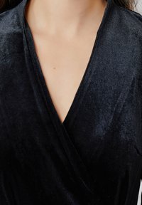 Un haut en velours noir avec un décolleté en V profond, une texture lisse et sans matériel ou embellissements visibles est exposé.