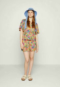 Conjunto colorido com padrão floral, apresentando um top cropped solto e calções, combinado com um chapéu de aba larga azul e sandálias bege.