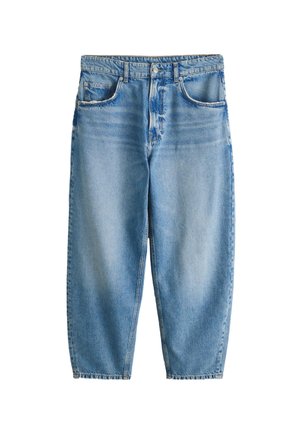 Mann trägt hellblaue, locker sitzende Jeans und schwarze Sneaker mit niedrigem Schaft und steht an einer beigen Wand.