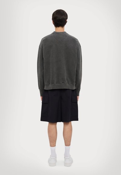 Grauer oversized Sweatshirt mit Rundhalsausschnitt, kombiniert mit schwarzen Cargo-Shorts, die zwei große Seitentaschen haben, und weißen Sneakers.