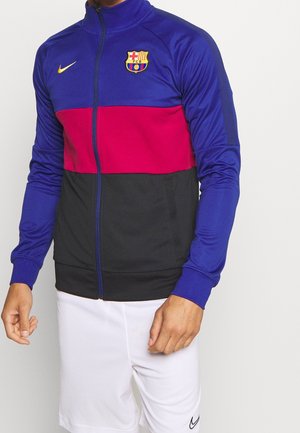 Kurtka piłkarska FC Barcelona, z niebieskimi, czerwonymi i czarnymi panelami, z zapięciem na zamek, wysokim kołnierzem i logo herbowym, wykonana z lekkiego materiału.