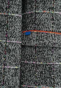 Čierno-biely rybia kosť vzor látky s viacfarebnými mriežkovými líniami, s vreckom lemovaným oranžovou hranou a malou modrou štítkom s dizajnom zatvoreného oka.