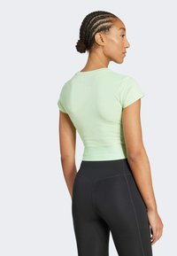 Camiseta verde claro ajustada de manga corta con dobladillo acanalado, combinada con leggings negros, vista desde atrás, destacando la textura suave.