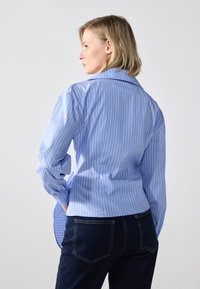 Lyseblå stripete skjorte laget av bomull, med krage og lange ermer, kombinert med mørkeblå denimjeans.