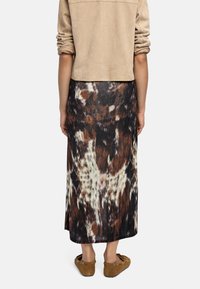 Beżowa zamszowa kurtka z podwiniętymi rękawami, w połączeniu z długą czarną spódnicą w brązowy i kremowy abstrakcyjny wzór oraz brązowymi butami wsuwanymi.