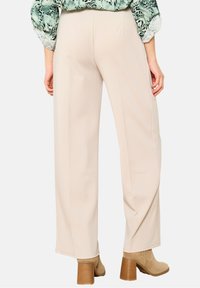 Béžové široké kalhoty s hladkou texturou, vysokým pasem a bočními švy, spárované s hnědými kotníkovými botami na blokovém podpatku.