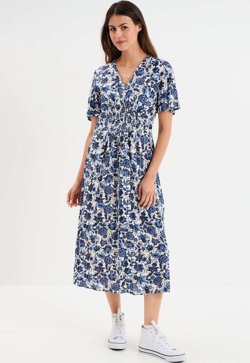 Blau-weißes Midi-Kleid mit floralem Druck, V-Ausschnitt, kurzen Ärmeln, gerafftem Bund und leichtem Stoff, kombiniert mit weißen Sneakers.
