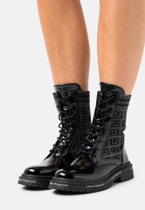 Zwarte combatlaarzen van lakleer met veterontwerp, bovenwerk van textiel met een logo-patroon en een dikke zwarte zool.