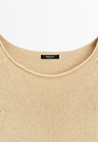 Maglione beige lavorato a maglia con scollo rotondo e un'etichetta nera con la scritta "Massimo Dutti Made in China" cucita all'interno del colletto.