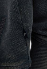 Donkerblauwe sweatshirt met een gestructureerde brei, zijzak en een klein blauw label met een wit embleem op de naad.