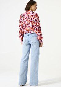 Blusa floral multicolorida con mangas largas, tejido suave y silueta fluida, combinada con jeans de pierna ancha de talle alto en azul claro.