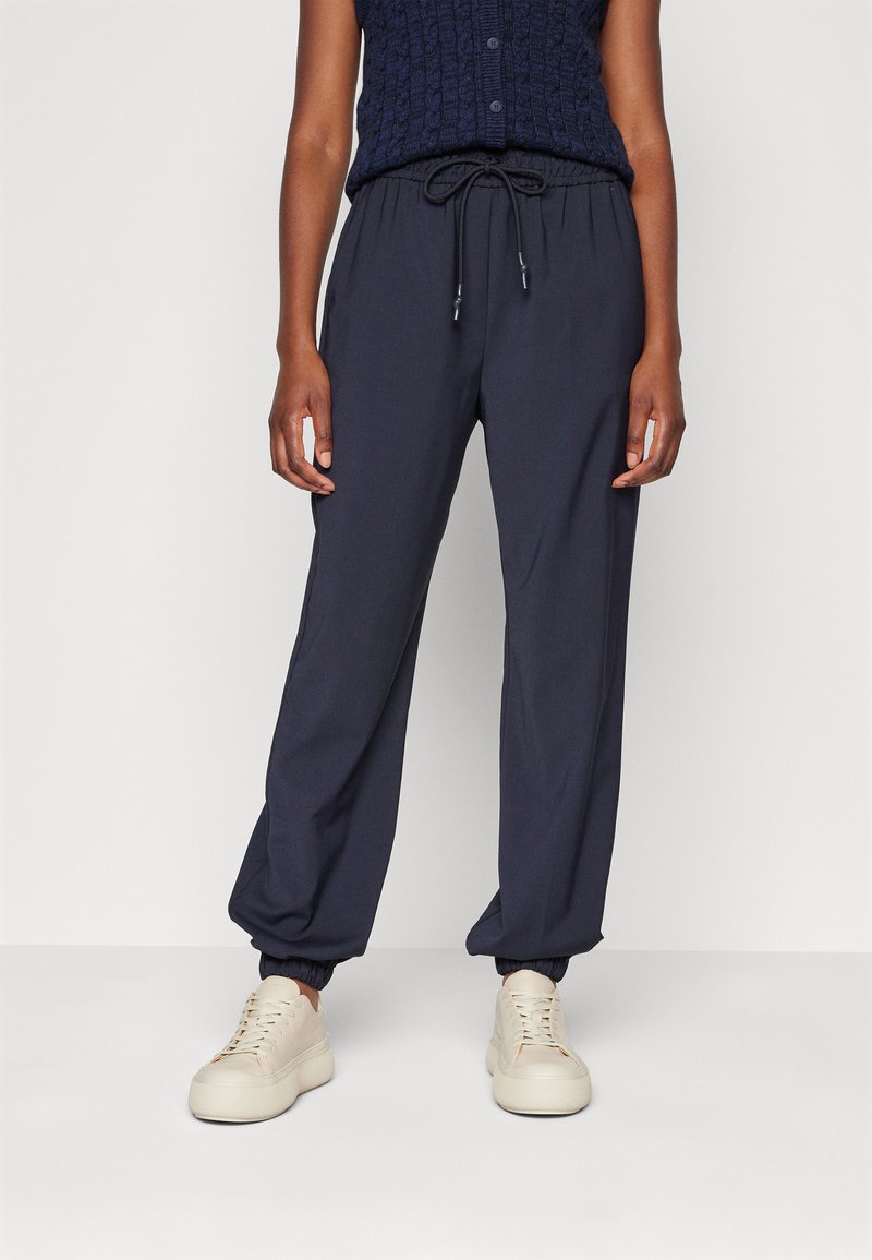 Granatowe joggerki z elastycznym pasem i sznurkiem, z mankietami na kostkach. W komplecie z jasnym obuwiem sportowym z wiązaniem.