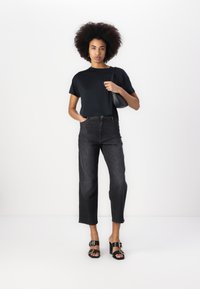 Μαύρο κοντό μπλουζάκι, ψηλόμεσα σκούρα τζην παντελόνια και μαύρες παντόφλες με αγκράφες. Μινιμαλιστικός σχεδιασμός με λευκό φόντο.