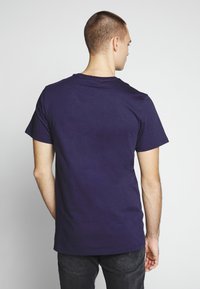 Camiseta de algodón azul marino con un cuello redondo clásico y mangas cortas, vista desde la parte de atrás. Textura suave, sin patrones ni gráficos visibles.