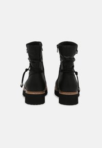 Botas de tobillo de cuero negro con un suave forro interior, cierre ajustable con cordón y un acento marrón en la suela. Diseño de tacón bajo.