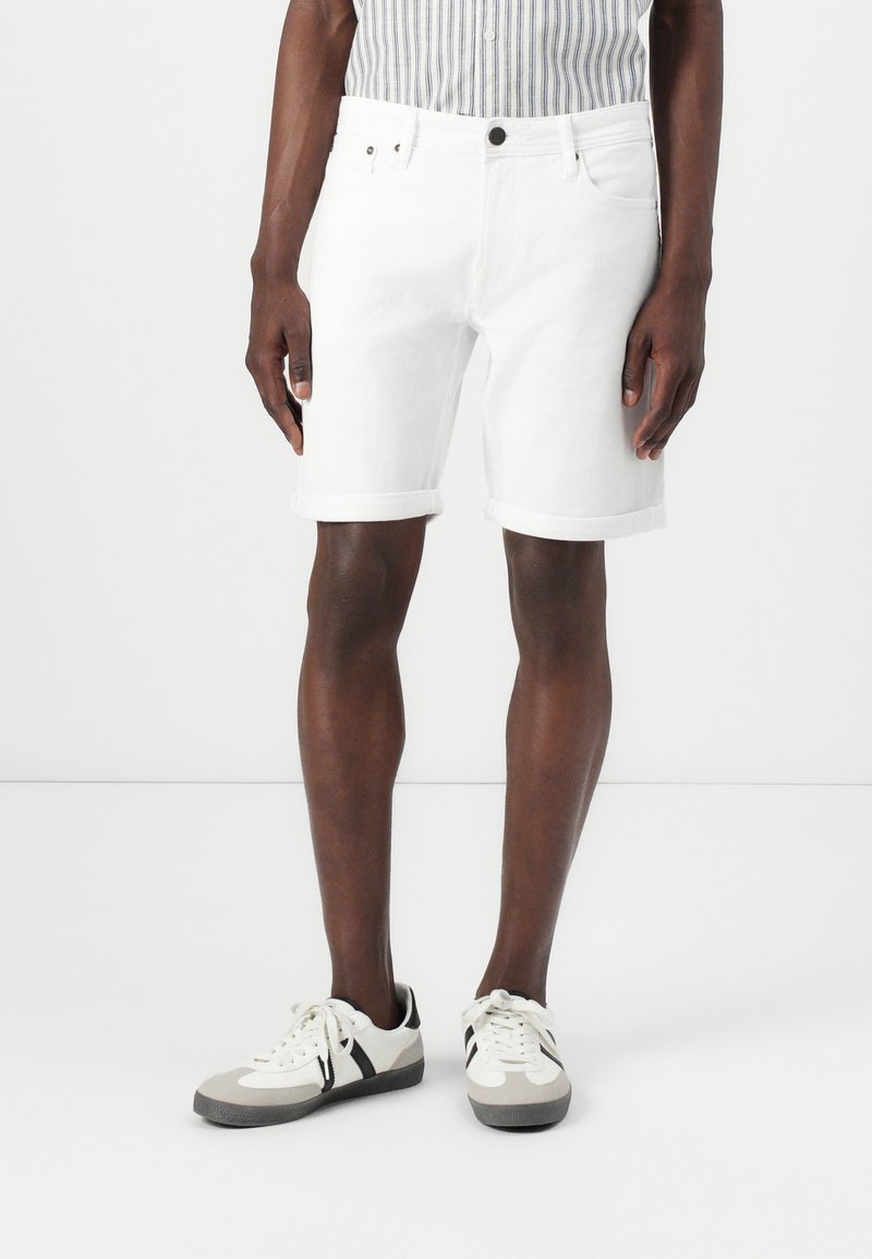 Hvide denimshorts med opsmøg, fem lommer og en sort knap. Kombineret med lysegrå og sorte sneakers.