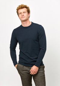 Mørkeblå langærmet T-shirt med rund hals, lavet af bomuld, har en glat tekstur og en tætsiddende pasform, kombineret med grå strukturerede bukser.