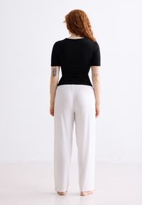 Zwart aangesloten T-shirt met korte mouwen, gecombineerd met losse witte wijde broekspijpen, gemaakt van een zachte stof en met een elastische tailleband, gezien vanuit de achterkant.