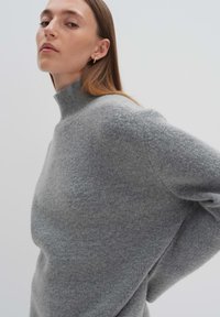 Hellgrauer Rollkragenpullover aus einem weichen, strukturierten Stoff. Mit einer lockeren Passform und überschnittenen Schultern für eine entspannte Silhouette.